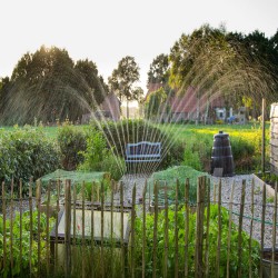 Irrigation sprinklers running over a Homestead garden at dusk